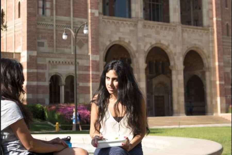 Two students chat near Shapiro Fountain, with Royce Hall in the background.